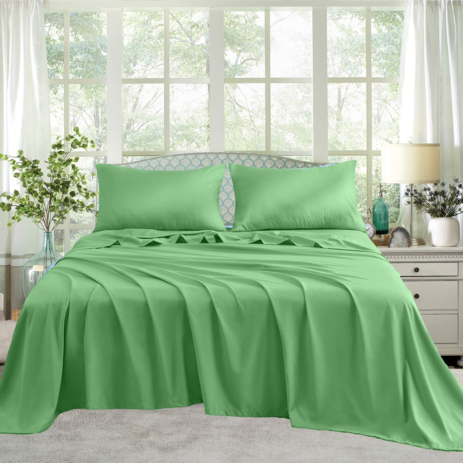 A neatly made bed with Green satin sheets and pillows
